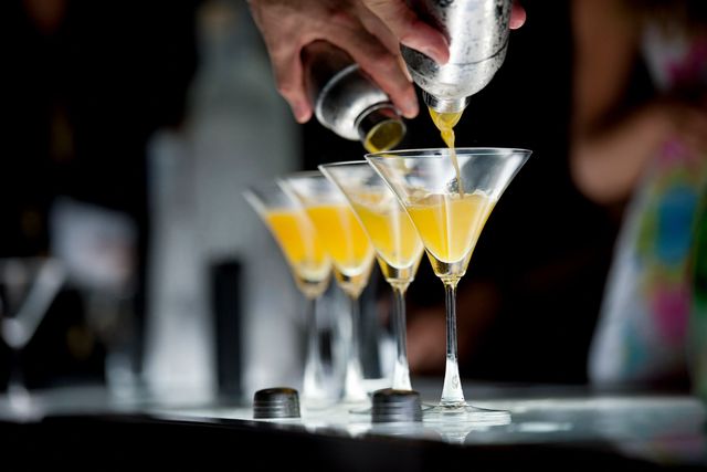 A person pouring orange juice into a martini glass.