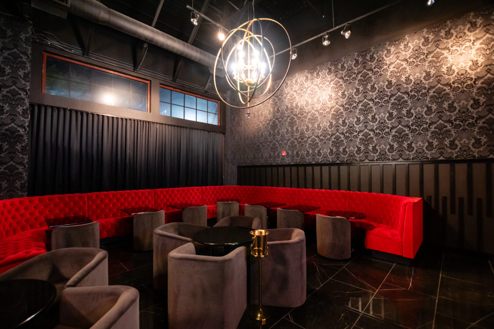 A dark luxury lounge with red couches and a chandelier.
