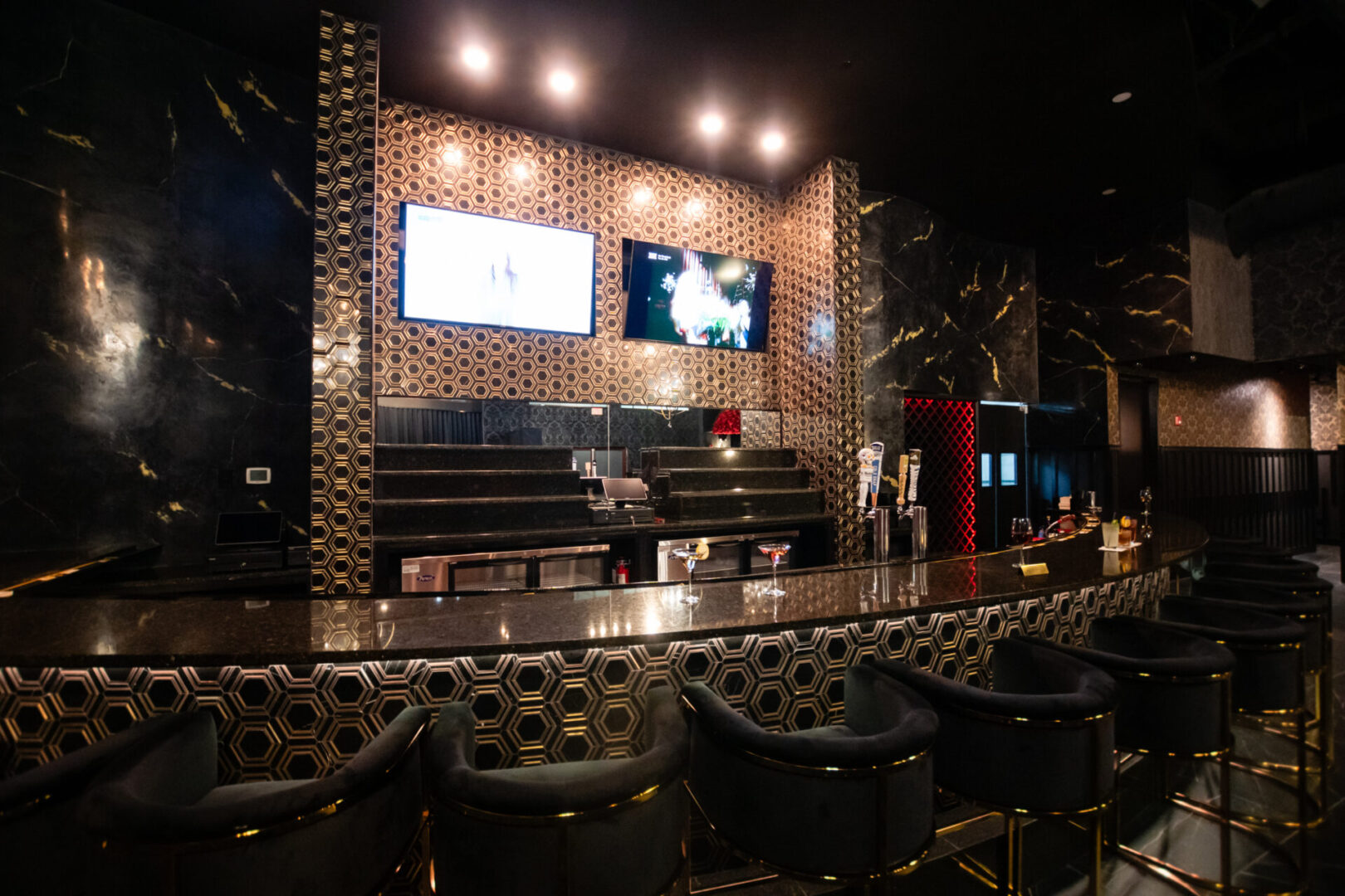 A black and gold luxury lounge with stools and a tv.