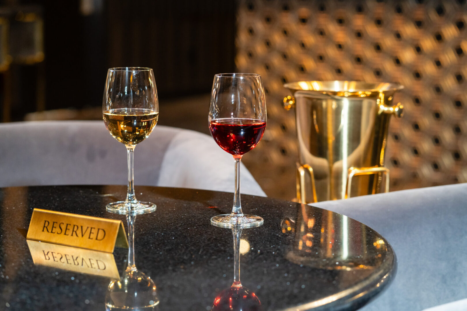 Two glasses of wine on a table next to a gold bucket in a luxury lounge.