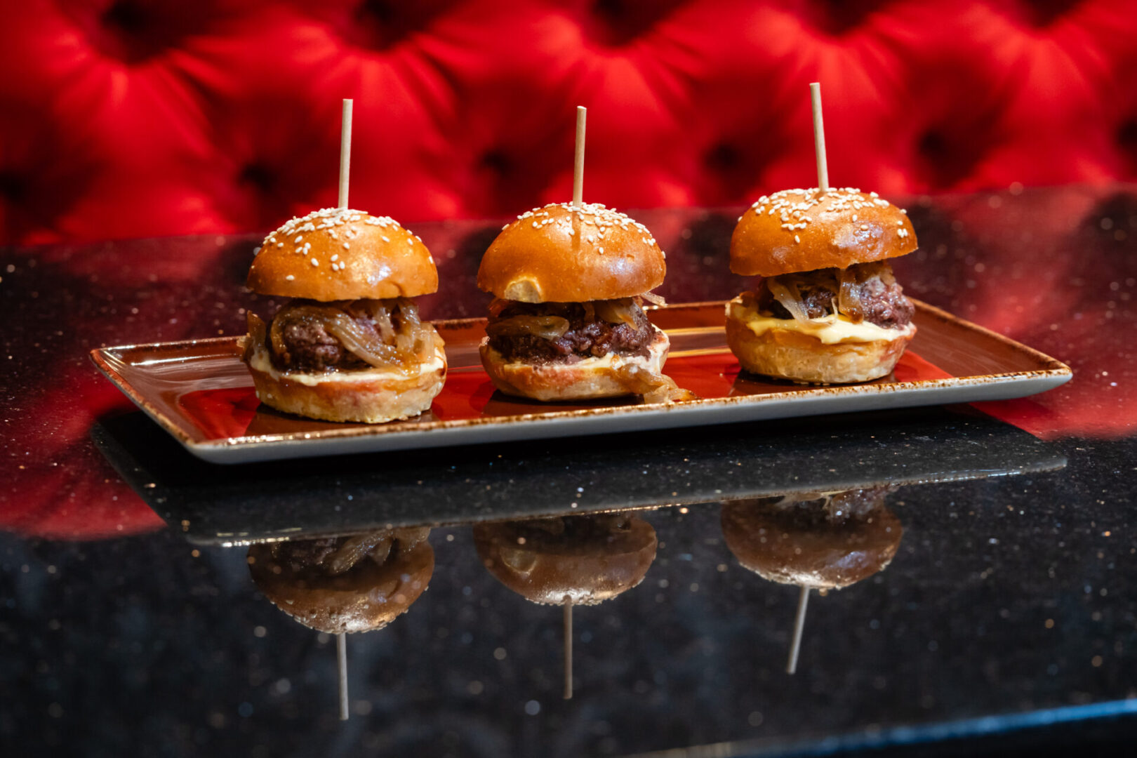 Three burger sliders are sitting on a tray in a luxury lounge.