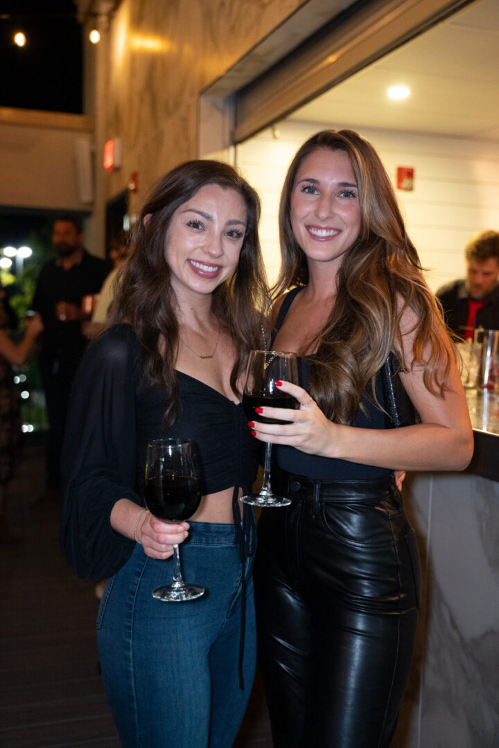 Two women standing next to each other in a luxury lounge, holding glasses of wine.