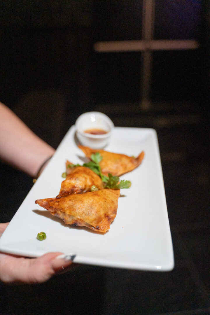 A person holding a plate of fried samosas in a luxury lounge.